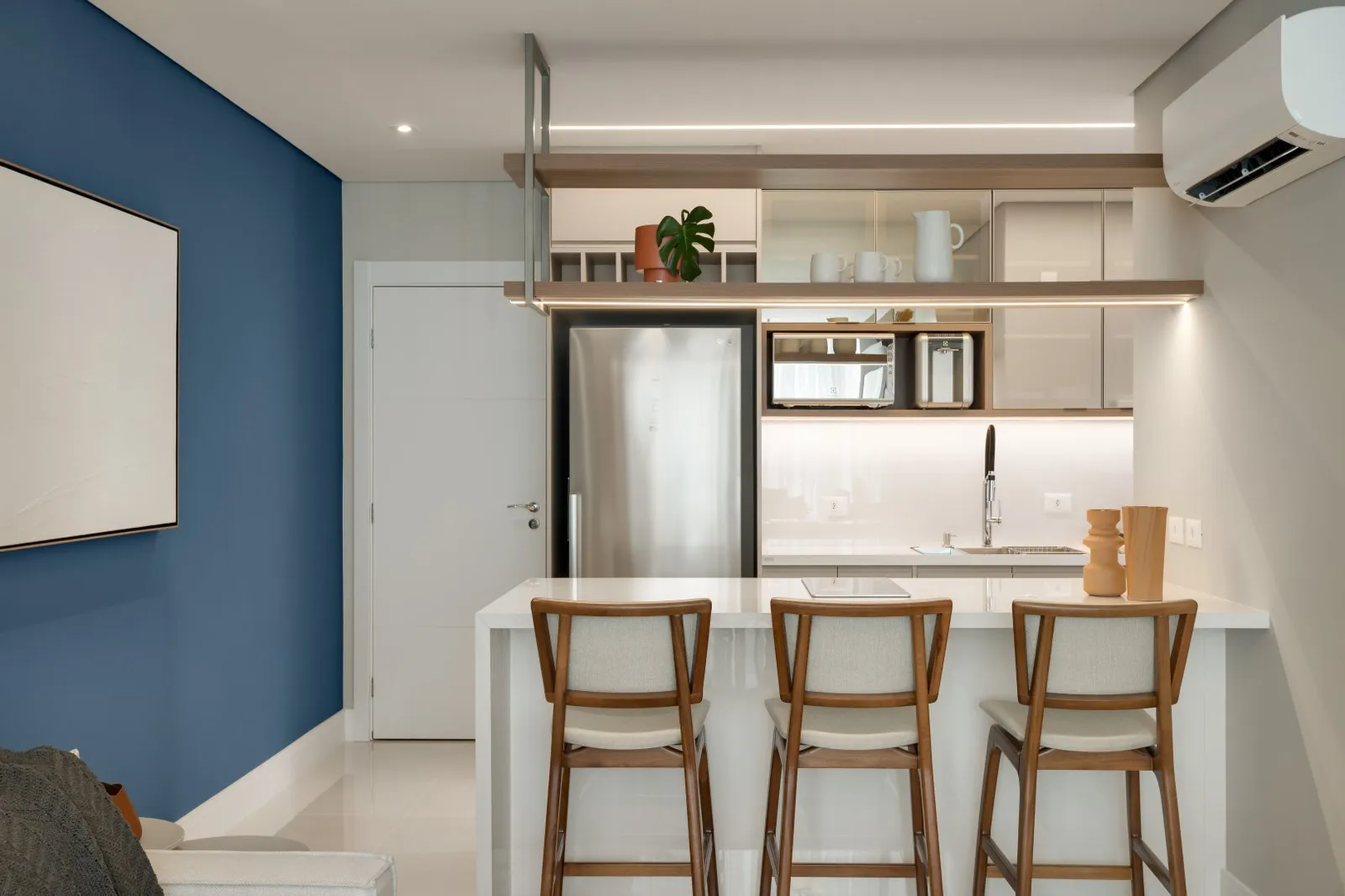 Cozinha integrada com bancada, banquetas de madeira e parede azul ao lado