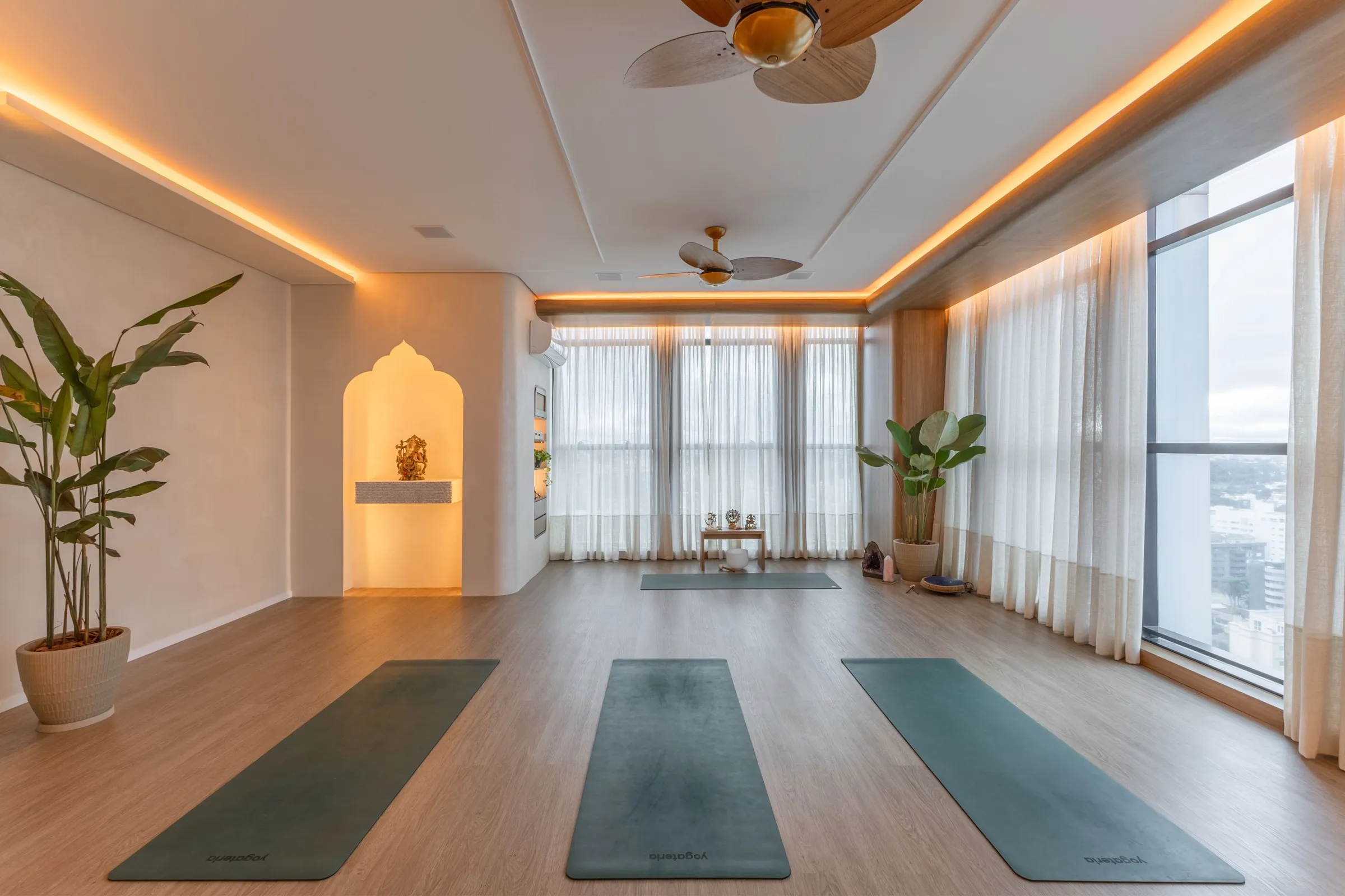 Sala de yoga com tapetes verdes, nicho iluminado e cortinas de linho
