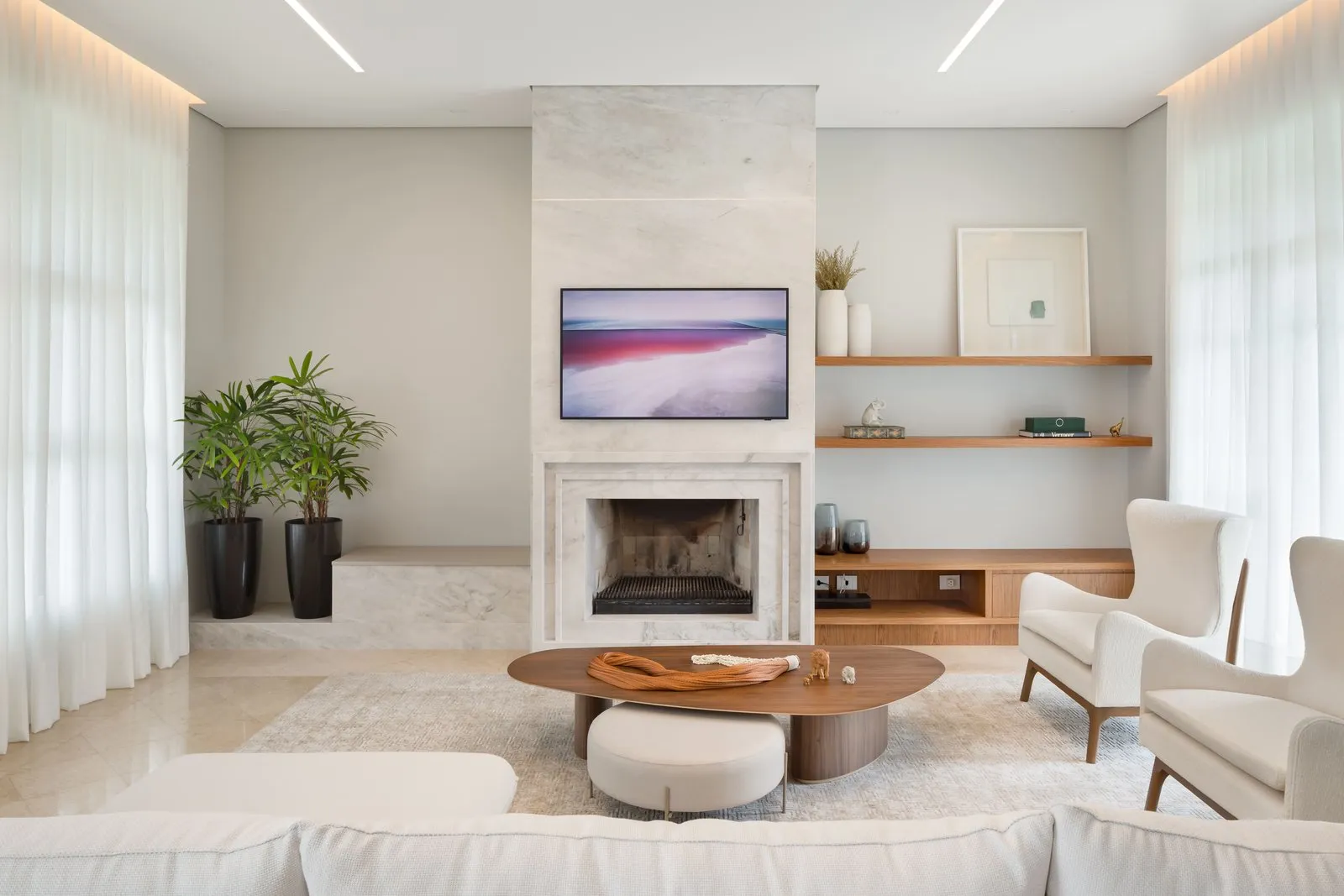 Sala de estar com lareira de mármore, TV e poltronas claras