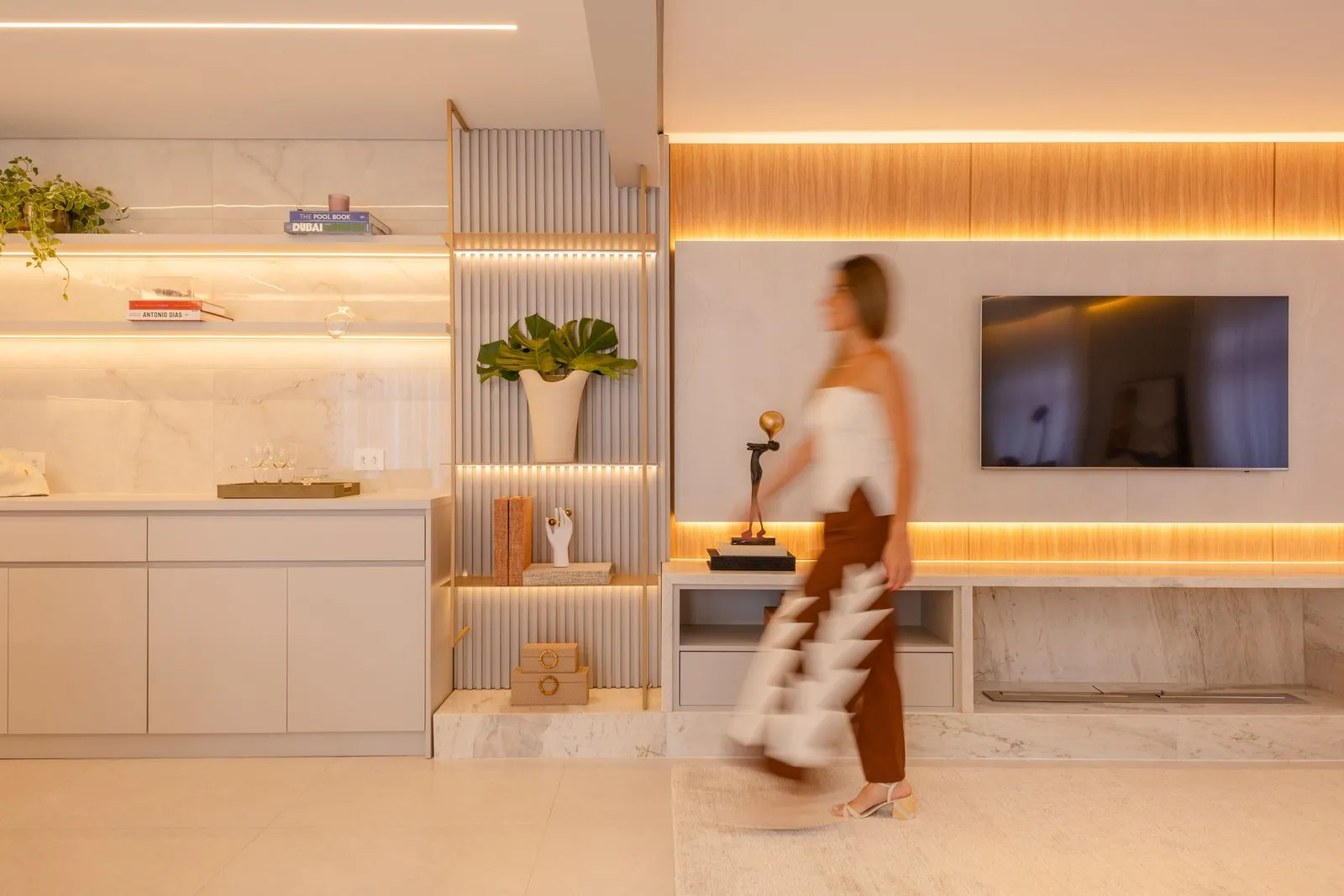Sala com estante ripada iluminada, painel de TV e bancada de mármore