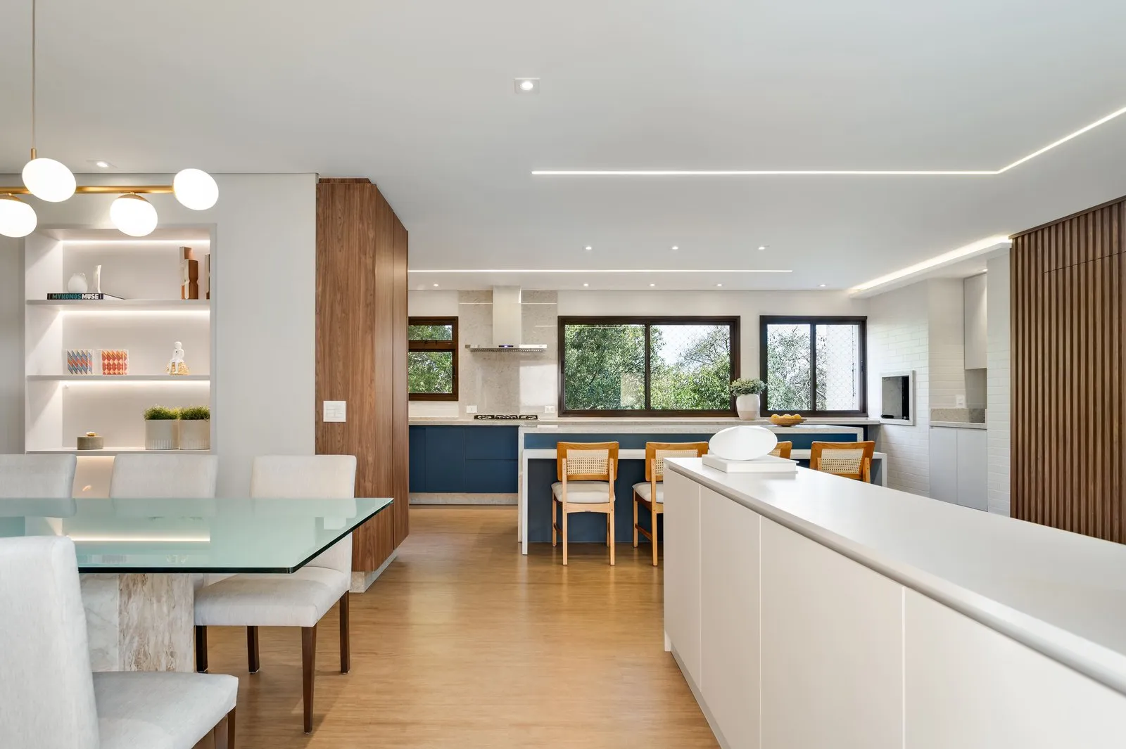 Cozinha e jantar integrados com marcenaria azul e piso de madeira