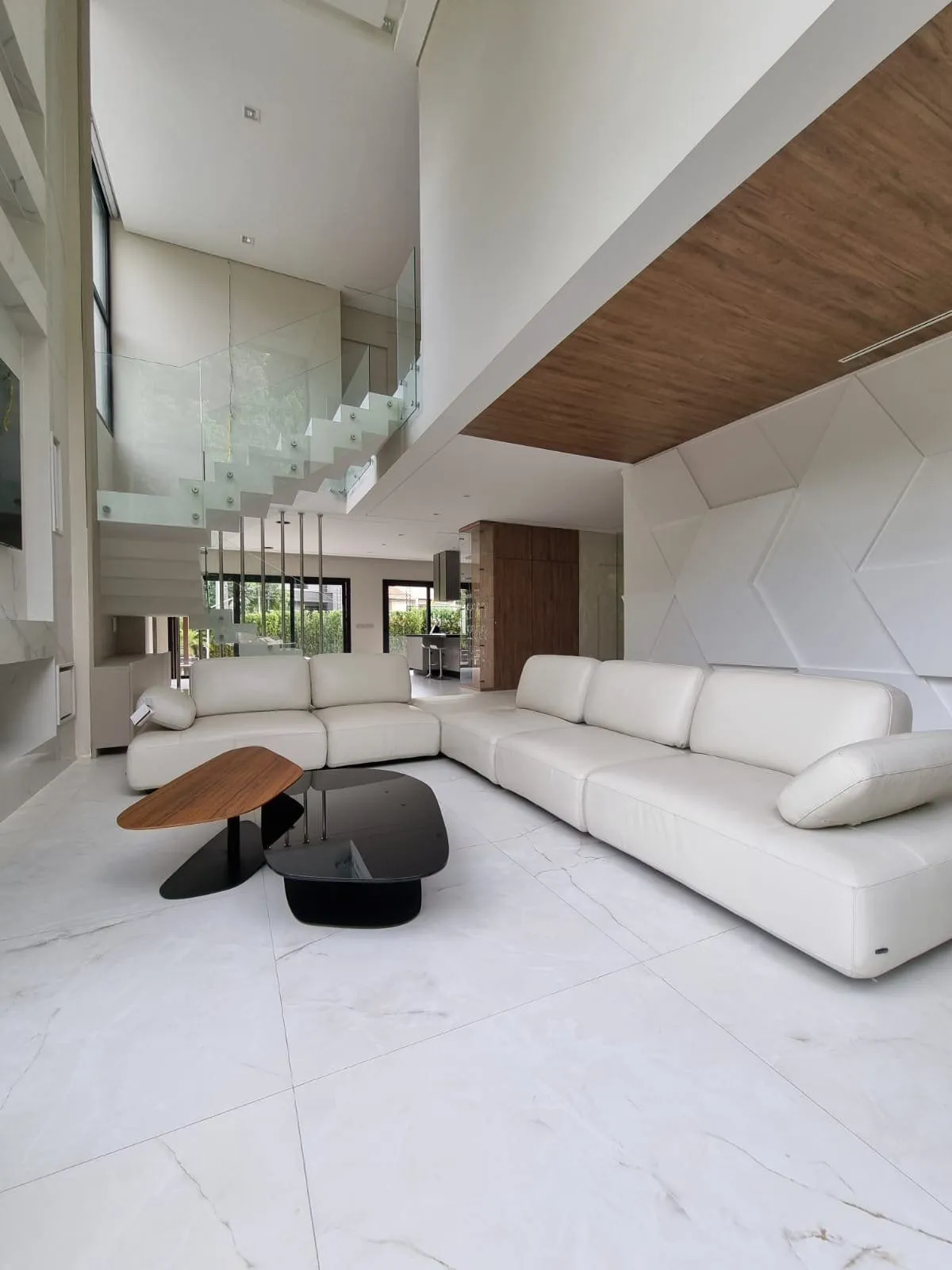 Sala de pé-direito duplo com sofá claro, escada de vidro e forro de madeira