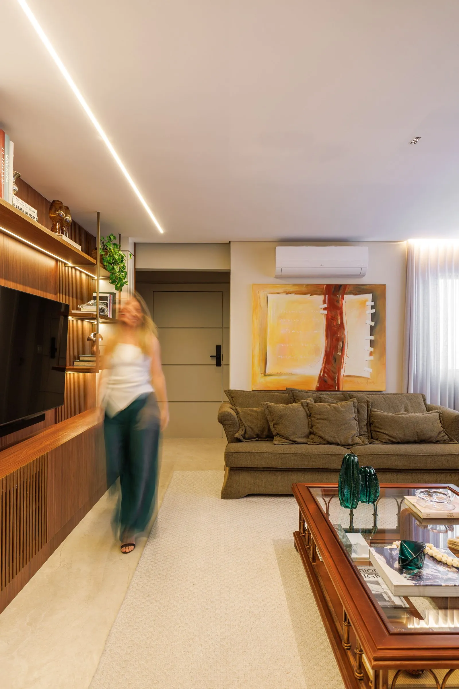 Sala de estar com estante de madeira iluminada, sofá verde-oliva e quadro grande