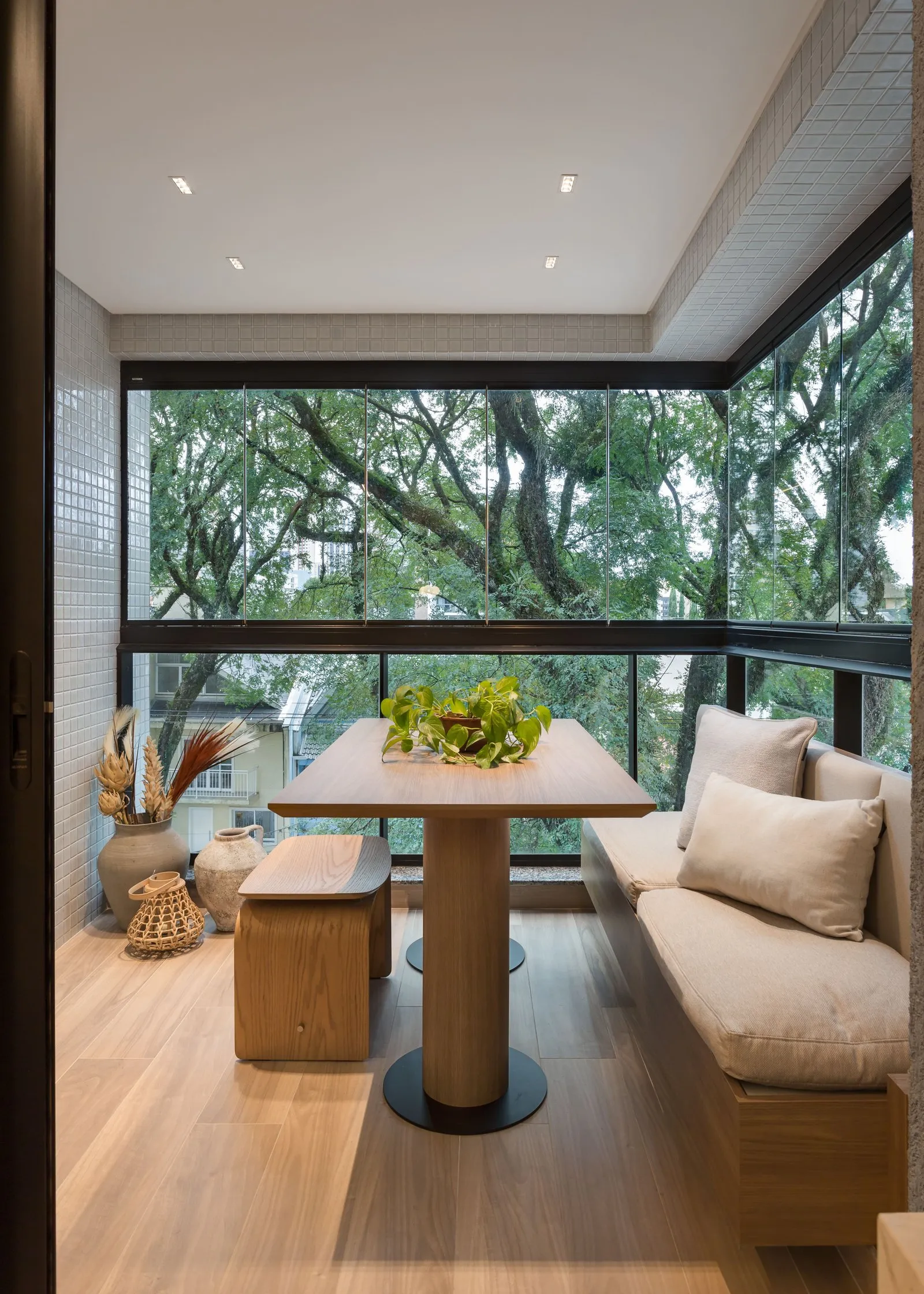 Varanda envidraçada com mesa, banco estofado e vista para as árvores