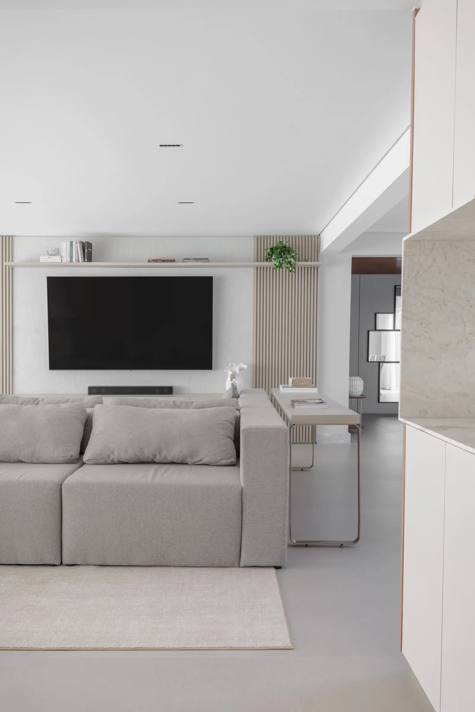 Sala de TV com painel ripado, sofá cinza e aparador fino