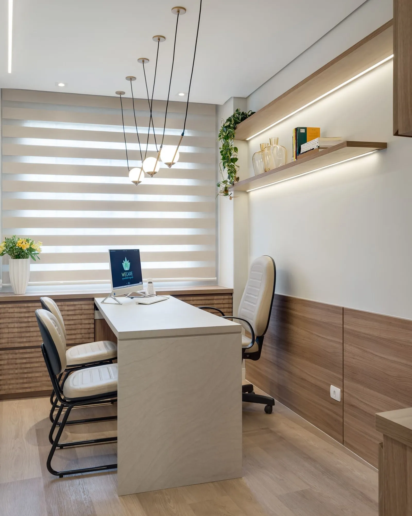 Sala de atendimento com mesa clara, pendentes de globo e prateleiras iluminadas