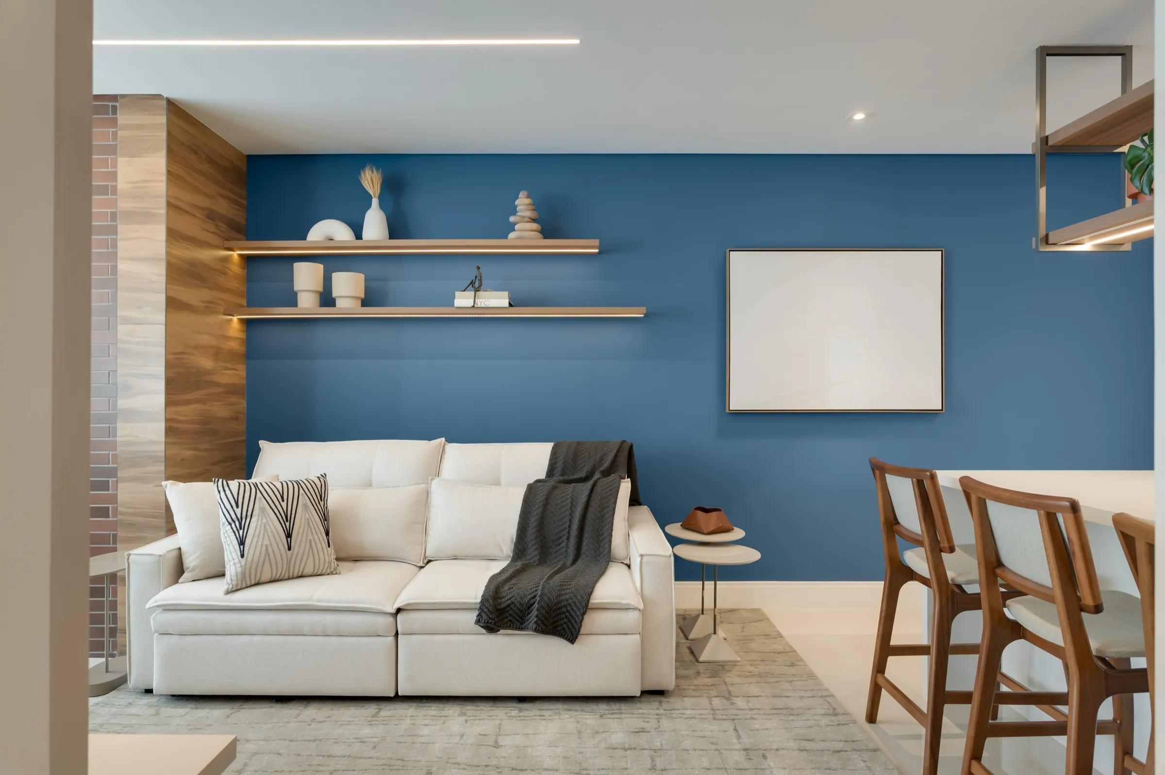 Sofá claro diante de parede azul com prateleiras iluminadas