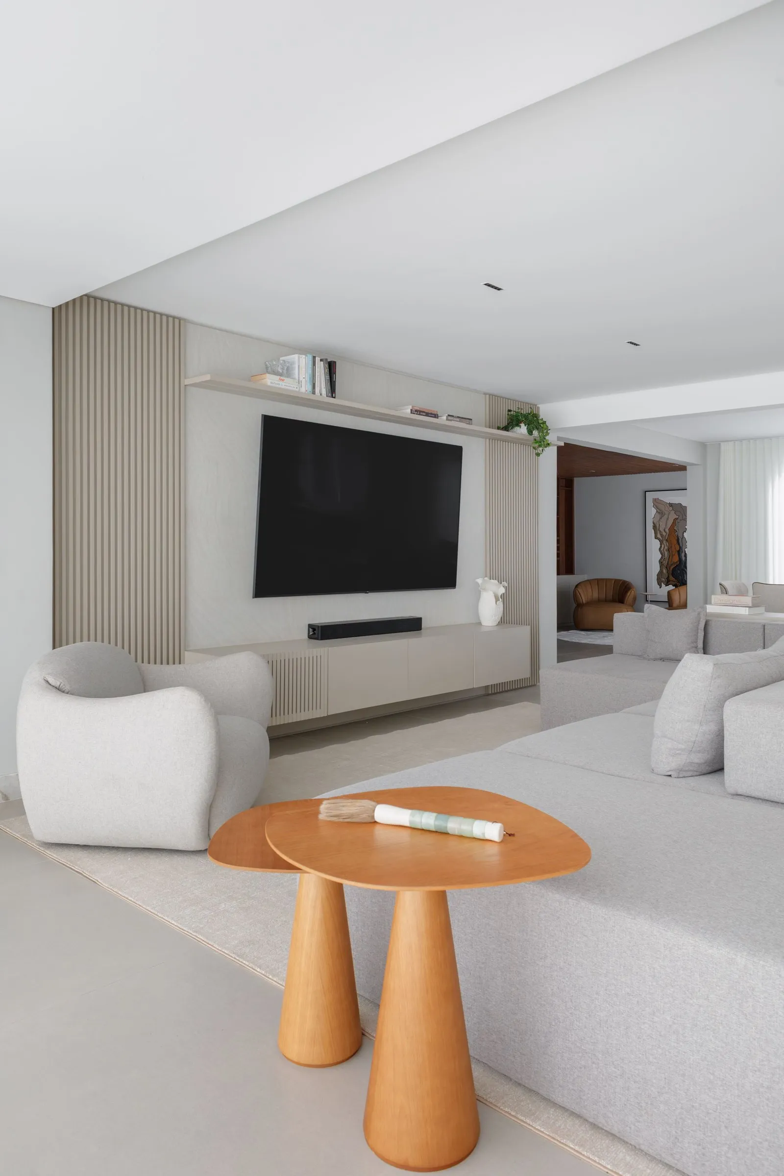 Sala com poltrona curva, mesas laterais de madeira e painel ripado atrás da TV