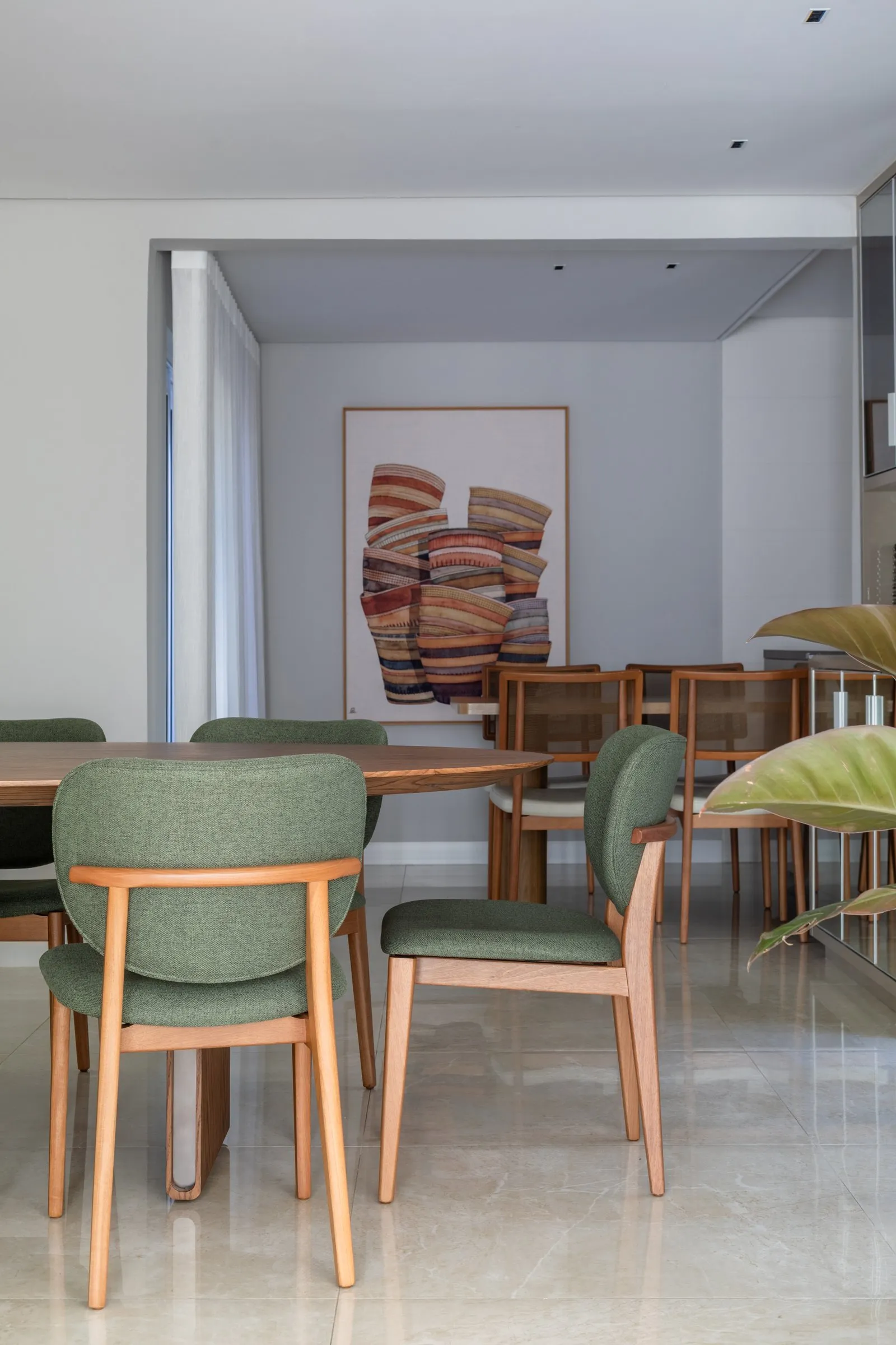 Sala de jantar com cadeiras verdes, mesa oval e quadro colorido