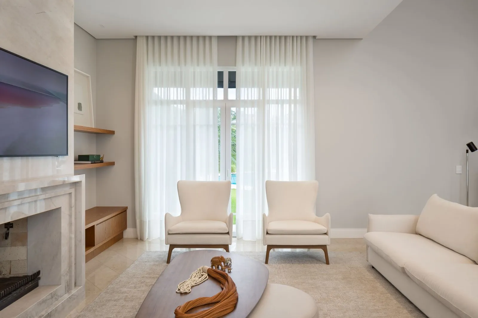 Poltronas claras diante de cortinas de voil e porta para o jardim