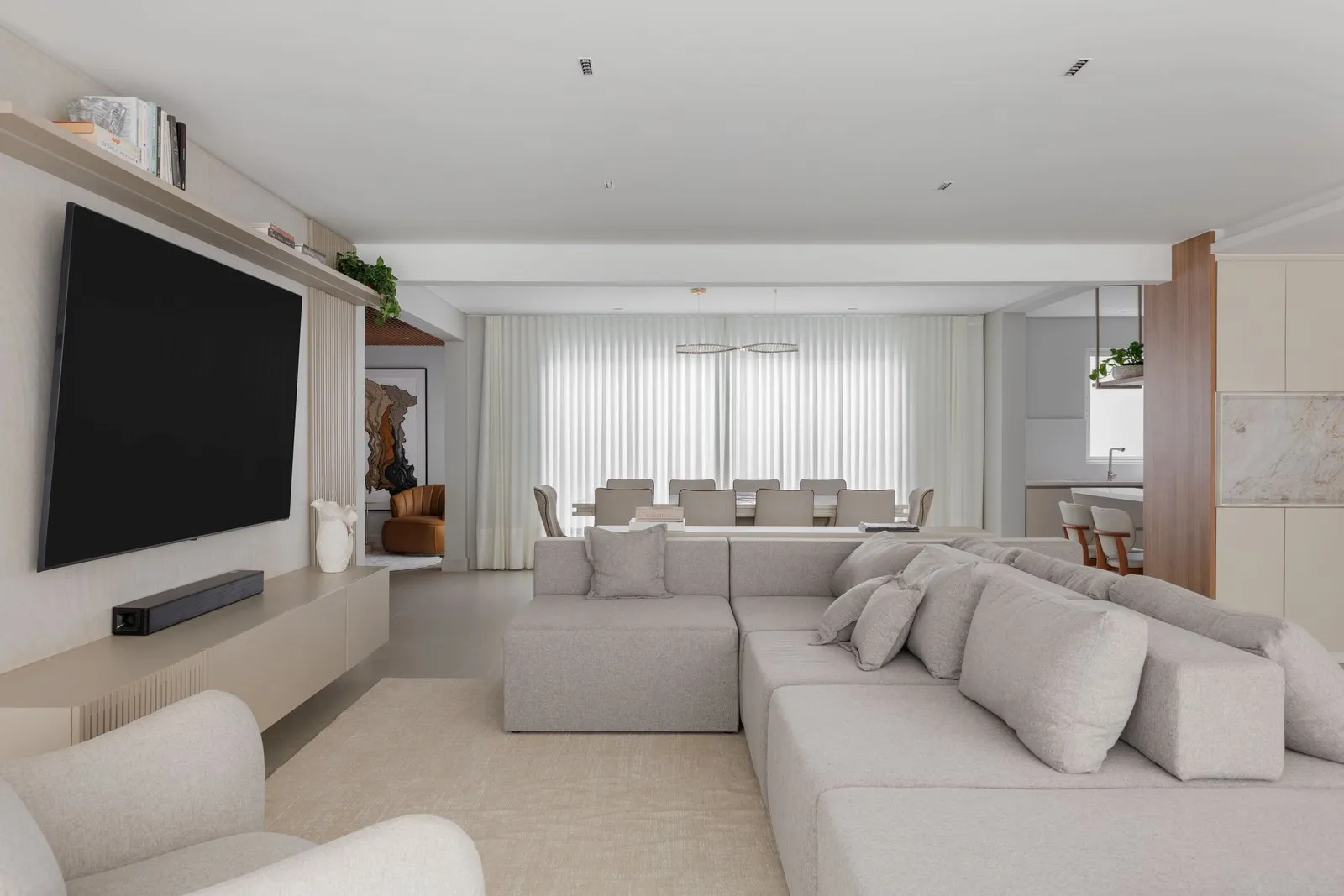 Sala de estar ampla com sofá modular, TV na parede e jantar ao fundo