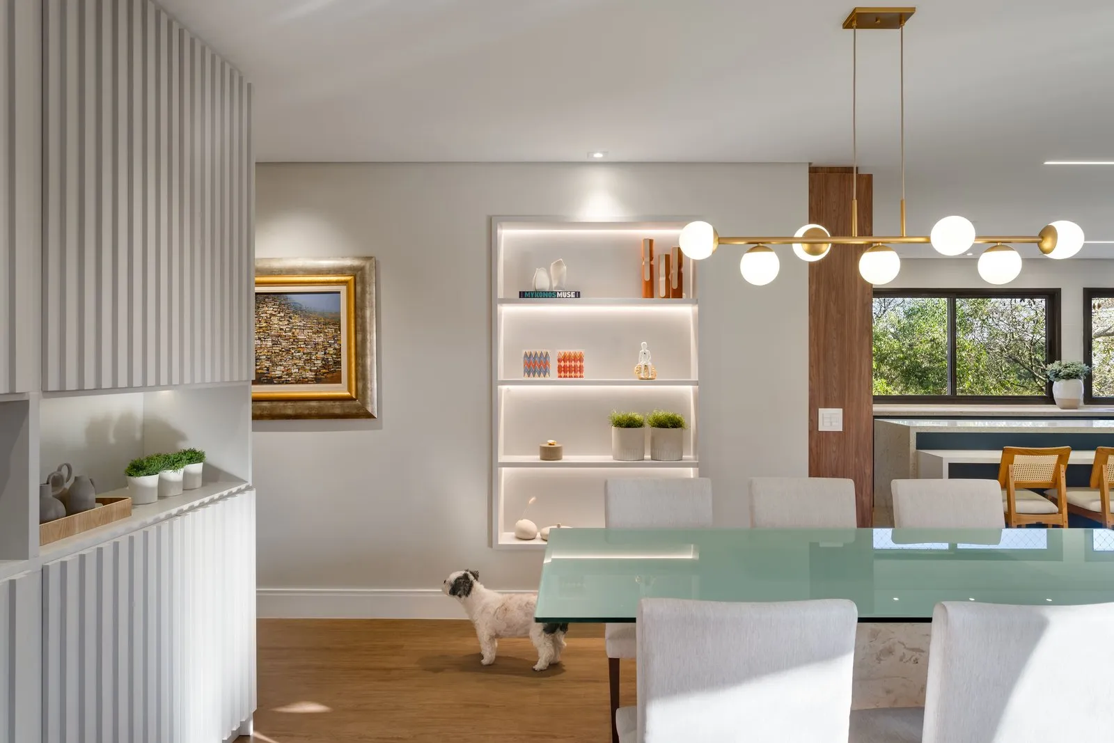 Sala de jantar com nicho iluminado, pendente dourado e mesa de vidro