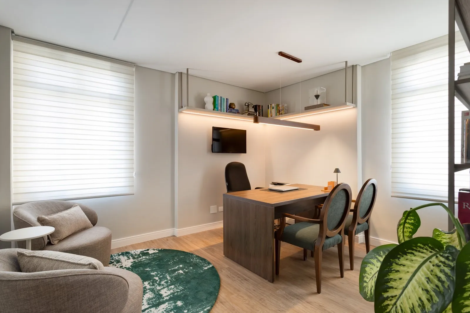 Sala de atendimento com mesa de madeira, cadeiras verdes e poltronas