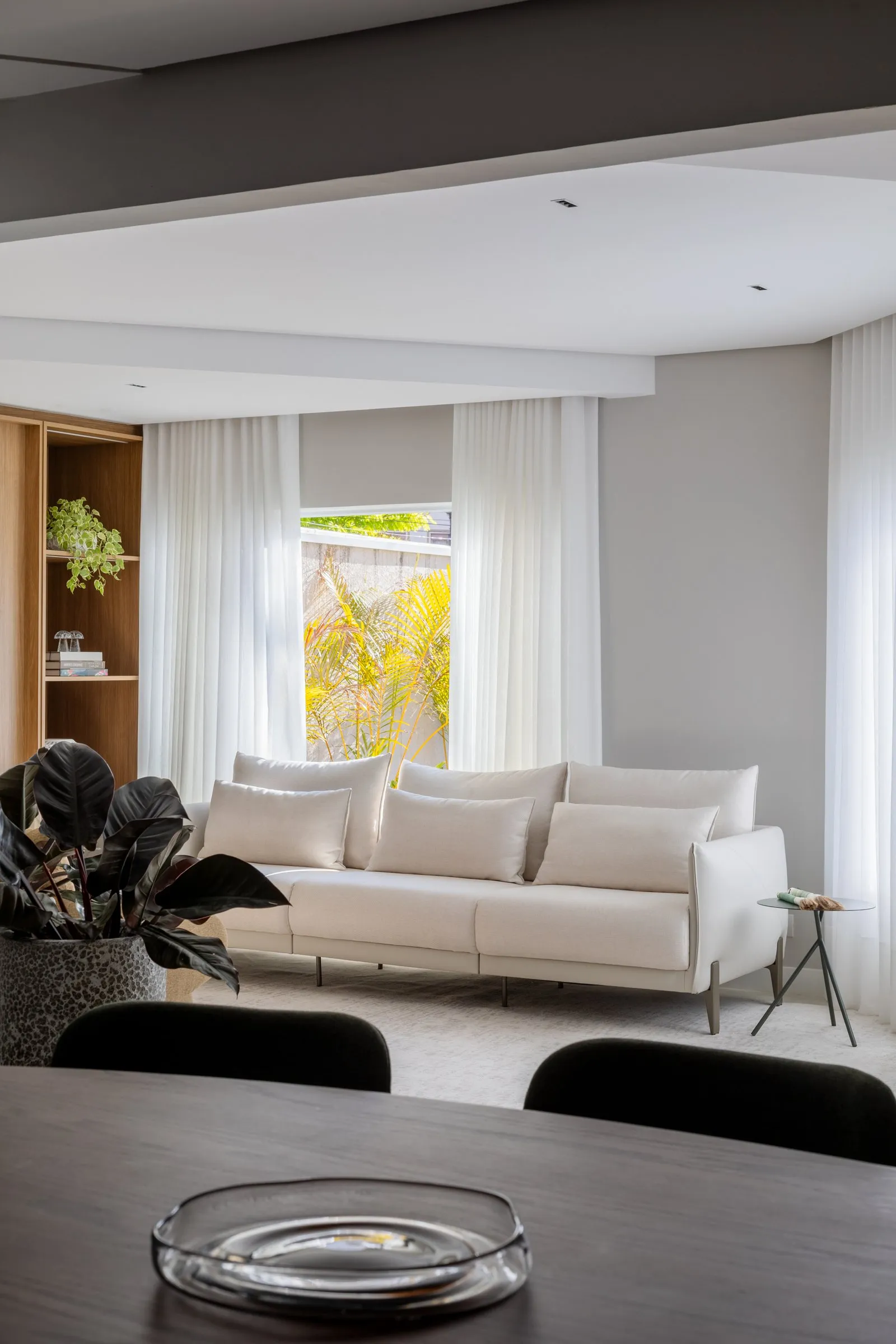 Sofá claro com cortinas leves visto por trás da mesa de jantar