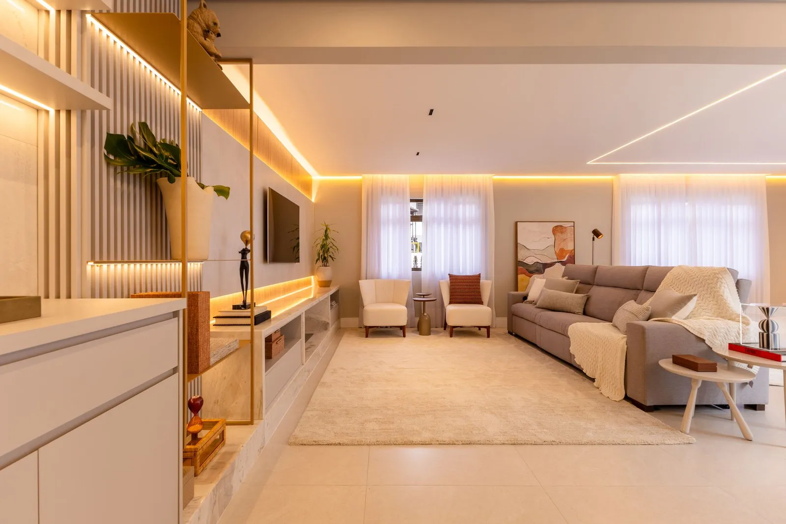 Sala de estar com sofá cinza, poltronas claras e fita de luz no teto