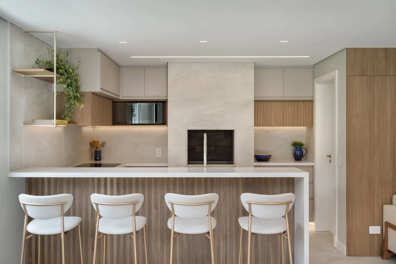 Cozinha integrada com bancada ripada, banquetas e churrasqueira em porcelanato