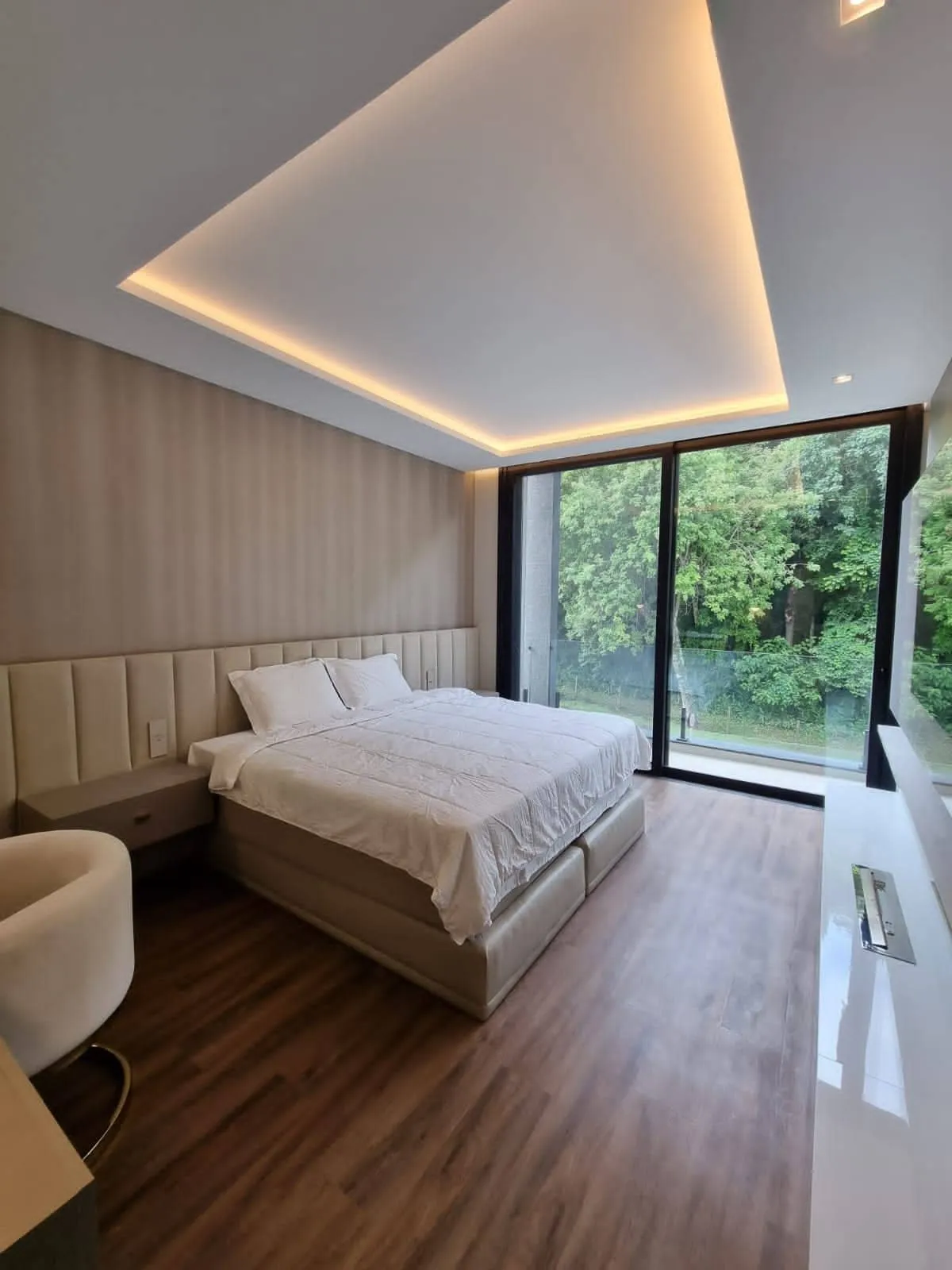 Quarto com cabeceira estofada, forro com luz embutida e vista para a mata