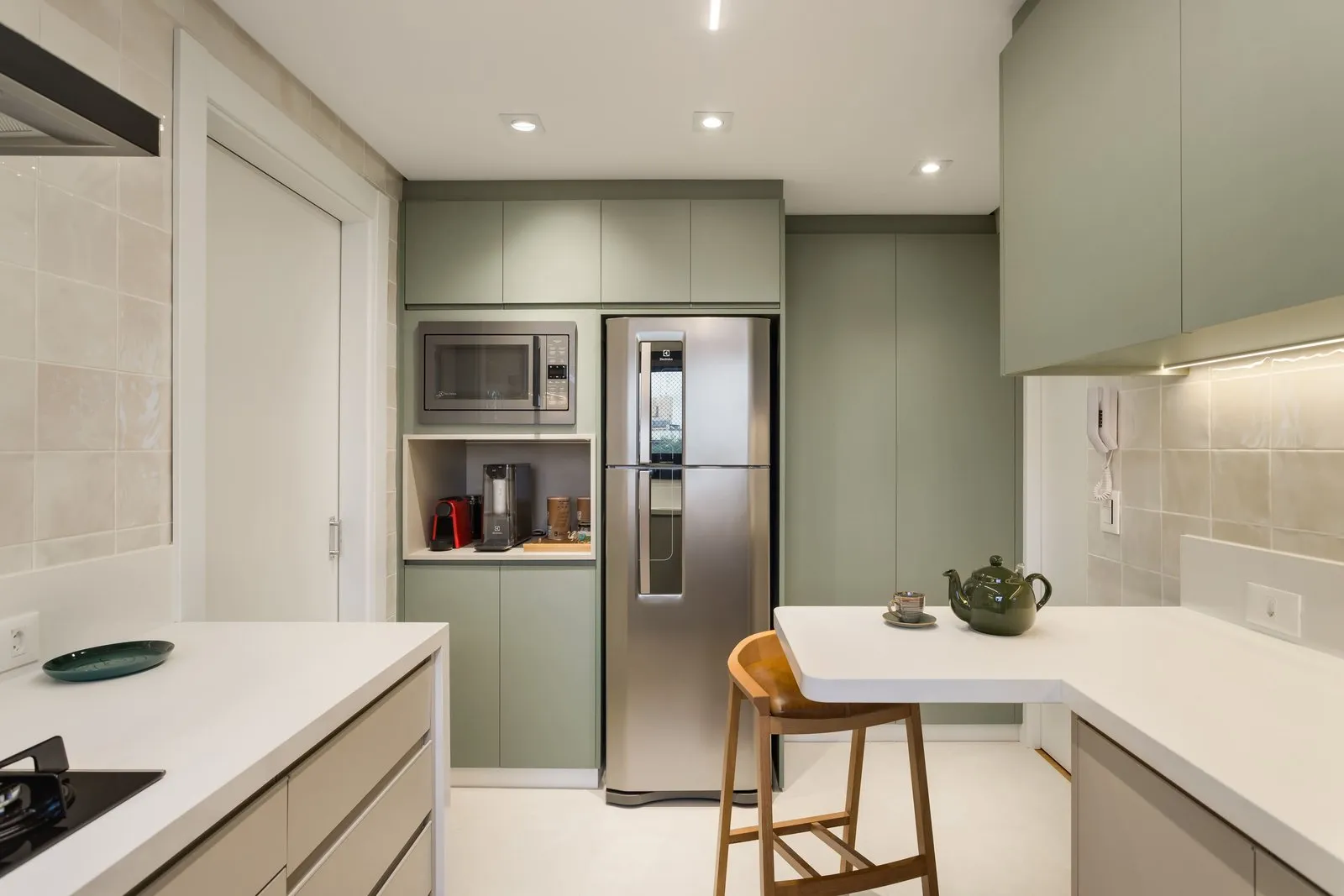 Cozinha com geladeira embutida em marcenaria verde e banqueta