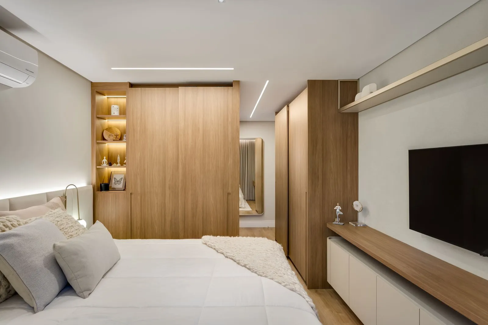 Quarto com armário de madeira, cama de roupa branca e painel de TV