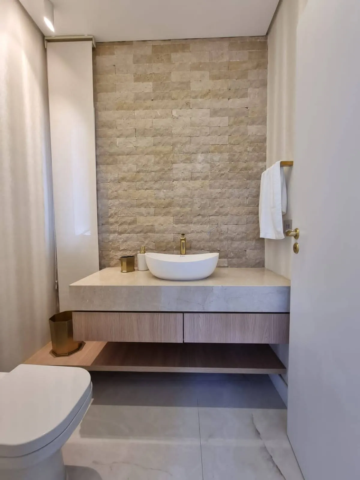 Lavabo com parede de pedra, bancada de mármore e cuba oval branca