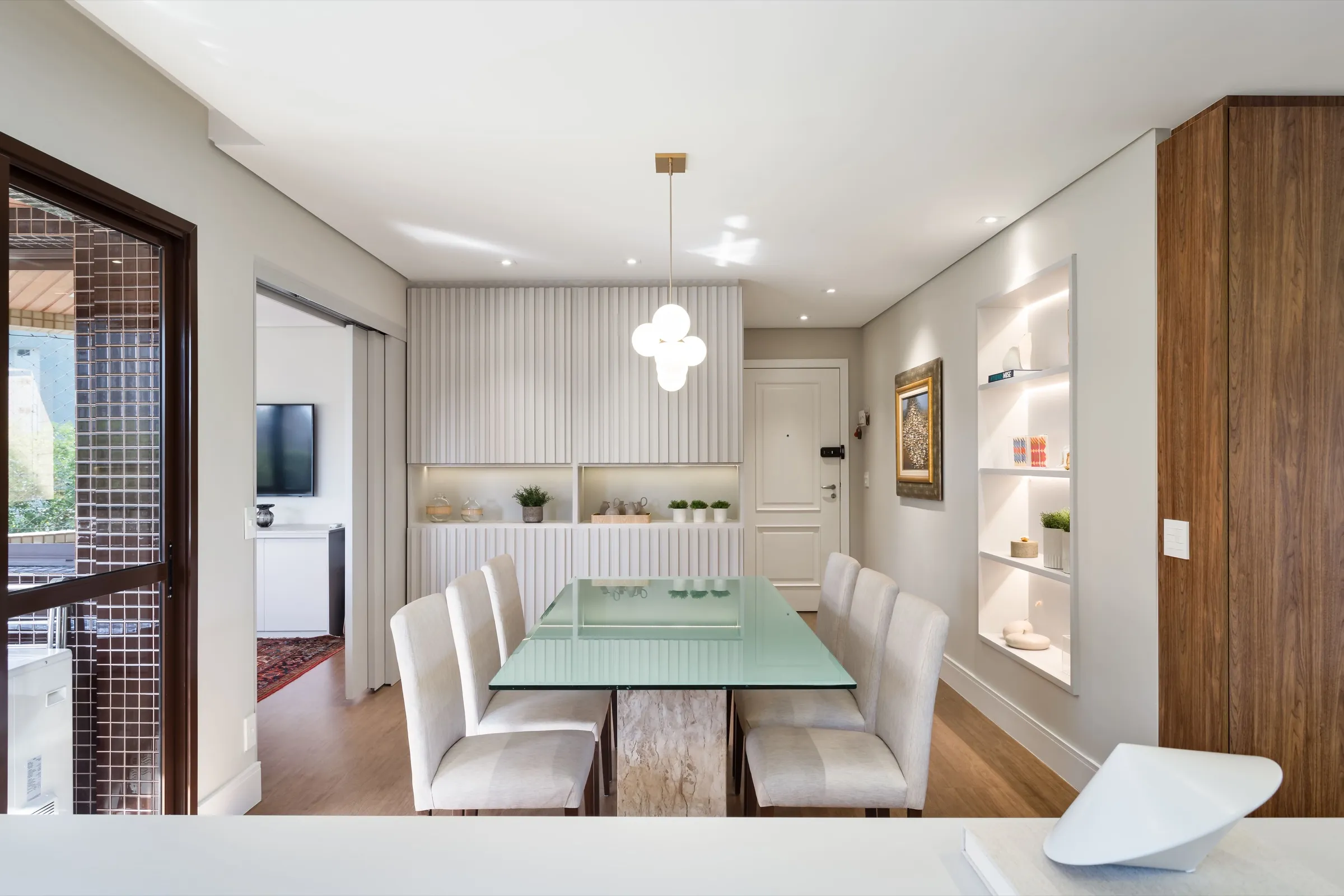 Sala de jantar com mesa de vidro, cadeiras estofadas e armário ripado