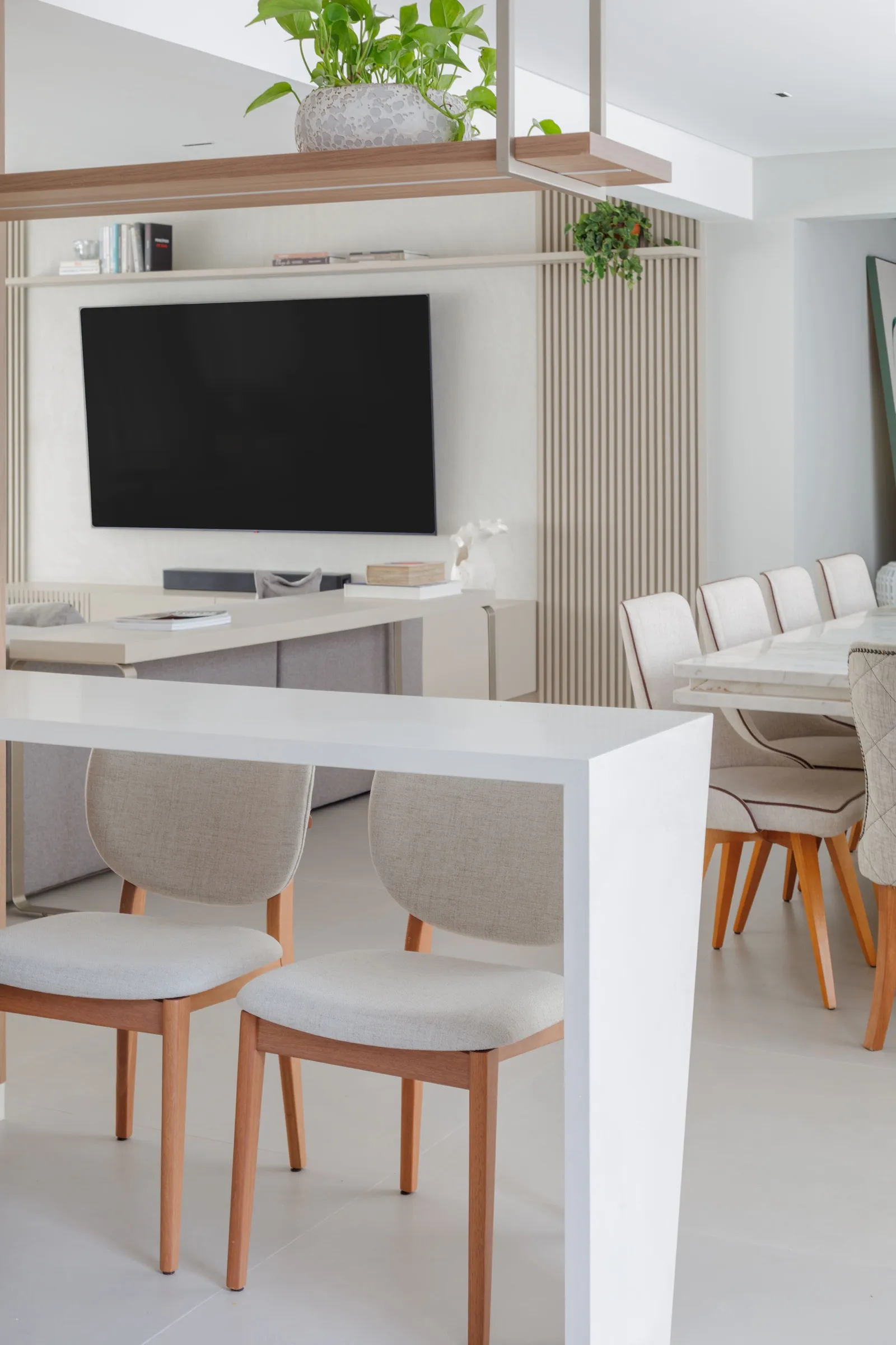 Sala de jantar e TV com painel ripado e bancada branca em primeiro plano