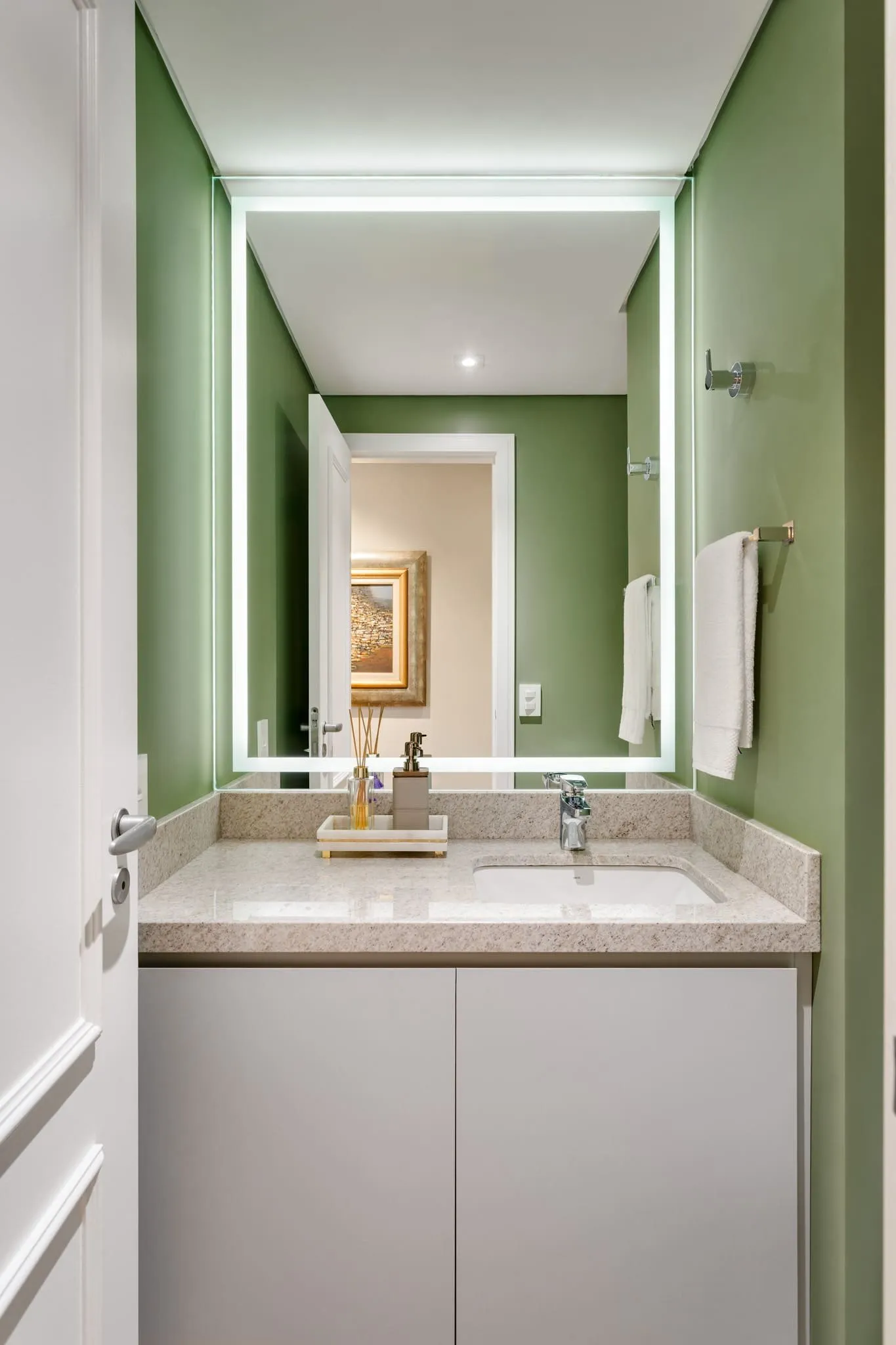 Lavabo com paredes verdes, espelho iluminado e bancada de granito