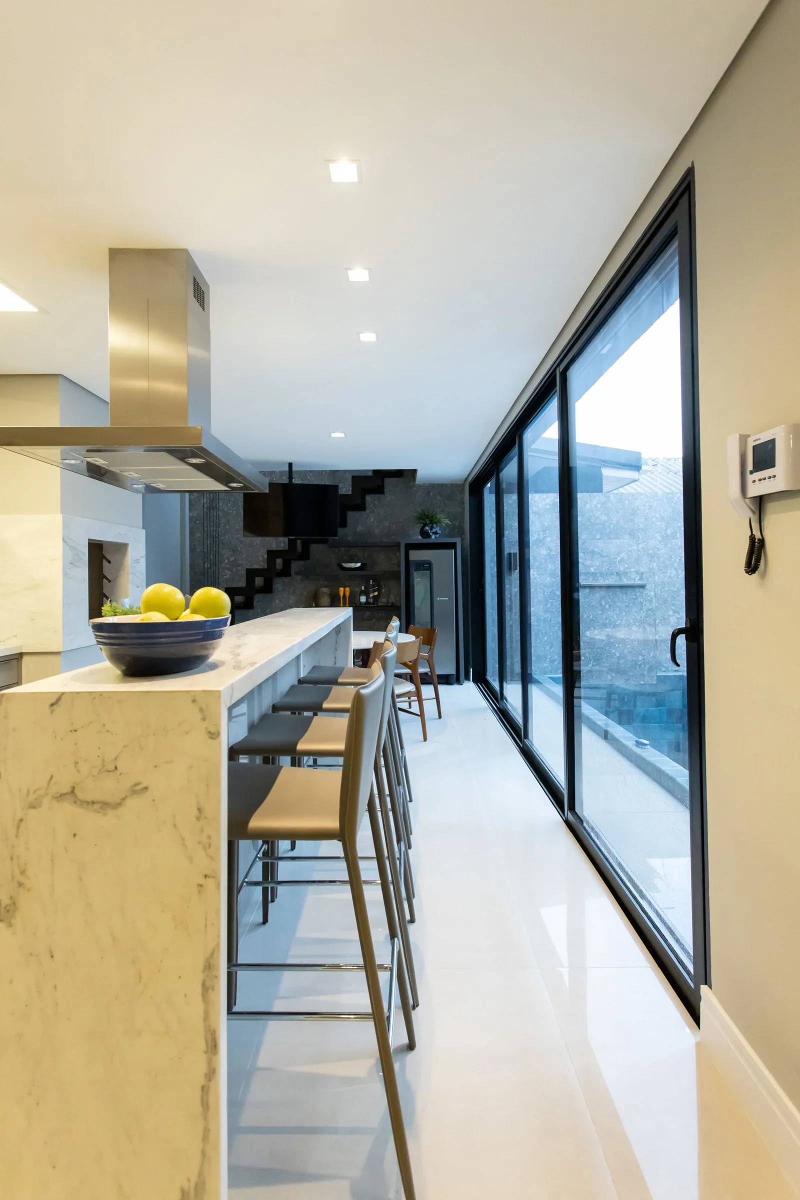 Cozinha com bancada de mármore, banquetas e janelas grandes para a piscina