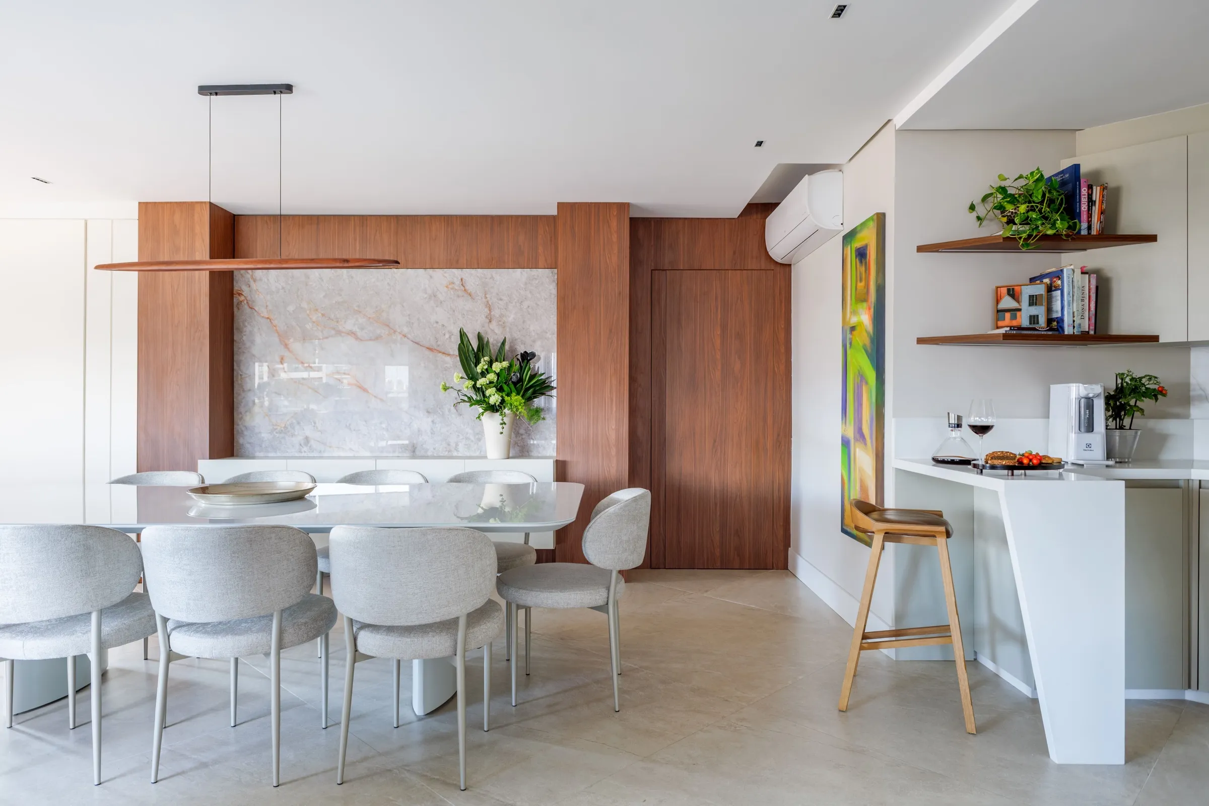 Sala de jantar com mesa branca, cadeiras estofadas e painel de pedra