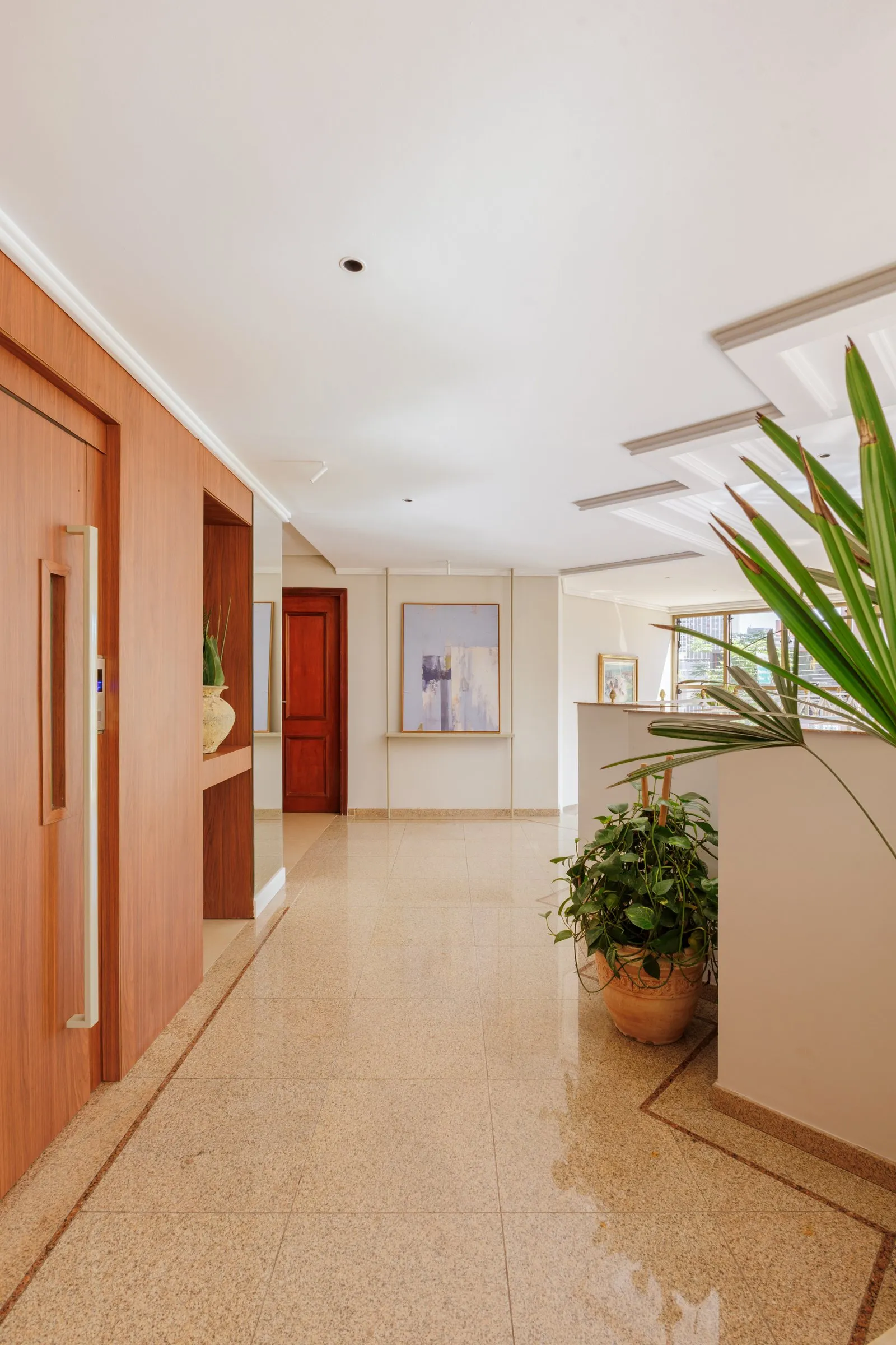 Corredor de circulação com piso brilhante, quadro ao fundo e plantas