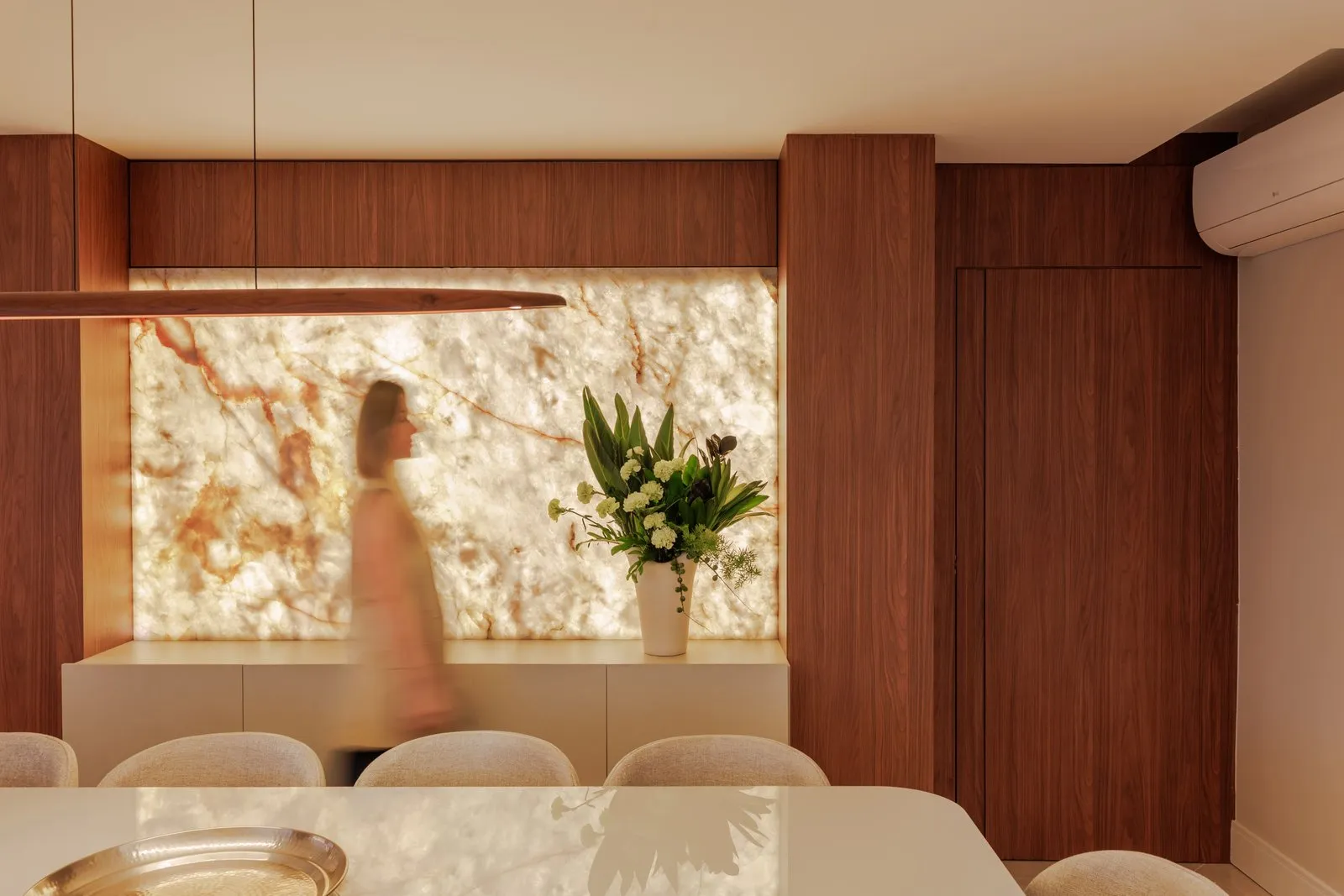 Sala de jantar com painel de pedra retroiluminada ao lado de armário de madeira