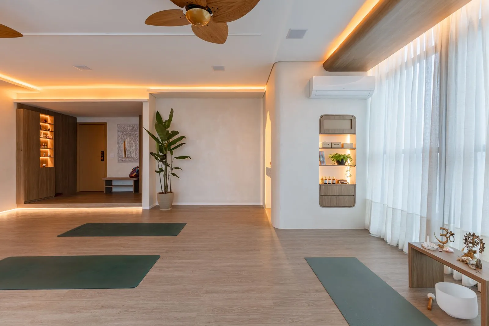 Sala de yoga com tapetes, bancada de altar e acesso à entrada ao fundo