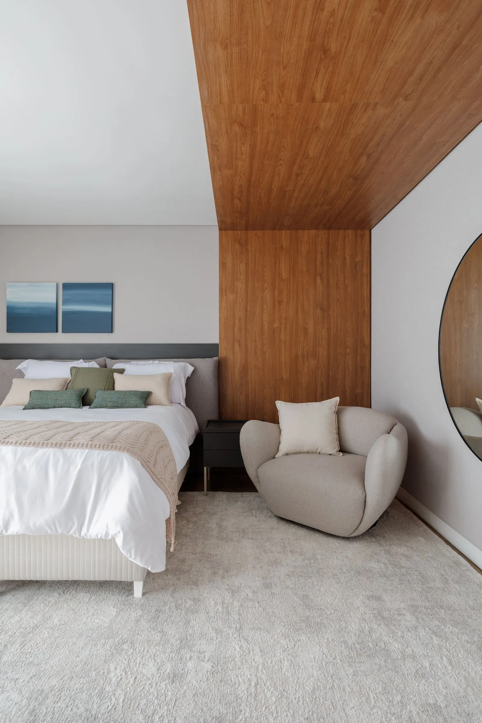 Quarto com cabeceira cinza, poltrona curva e painel de madeira no teto