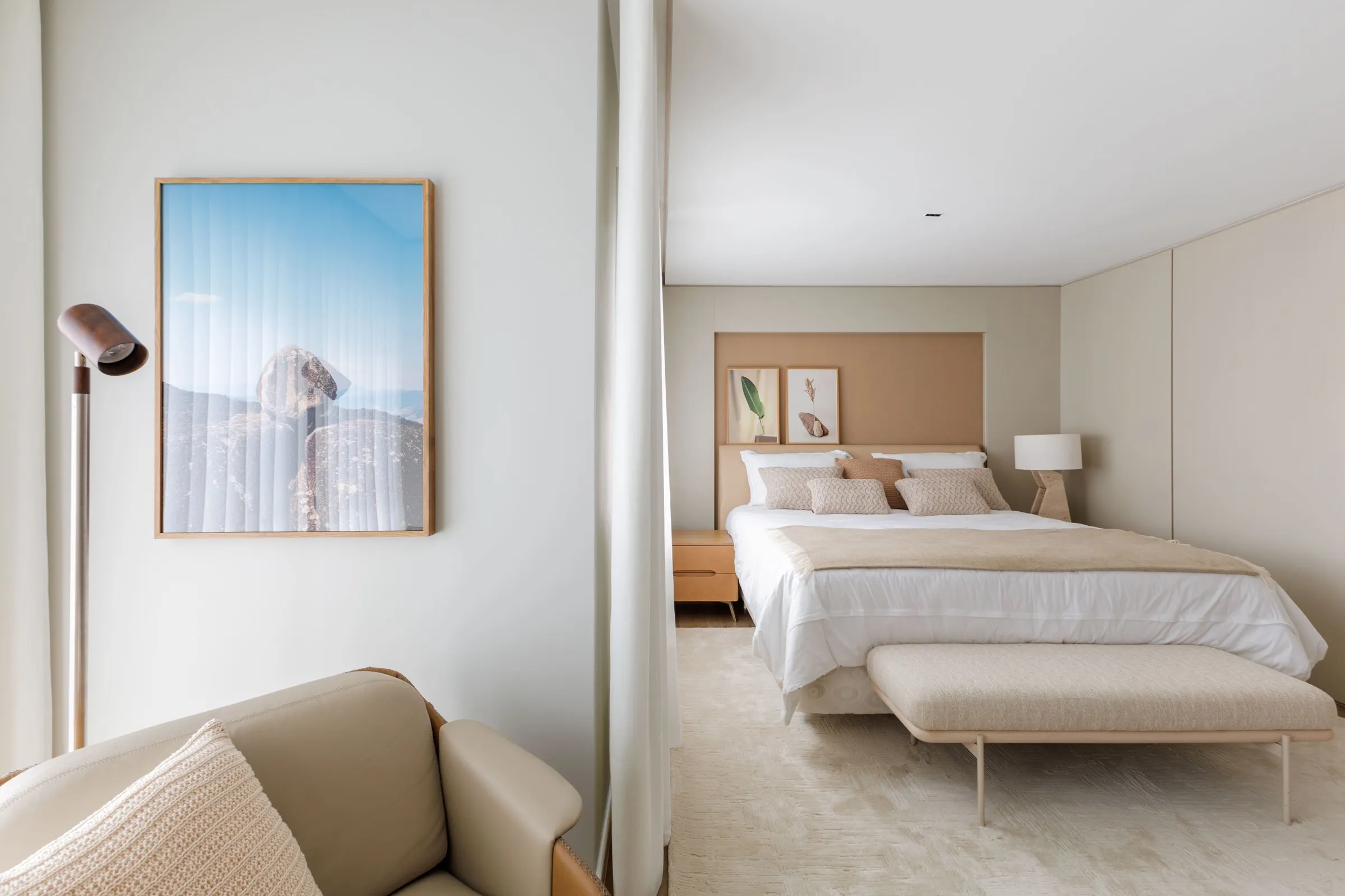 Suíte com cama, banco estofado, quadro grande e cortina ao lado