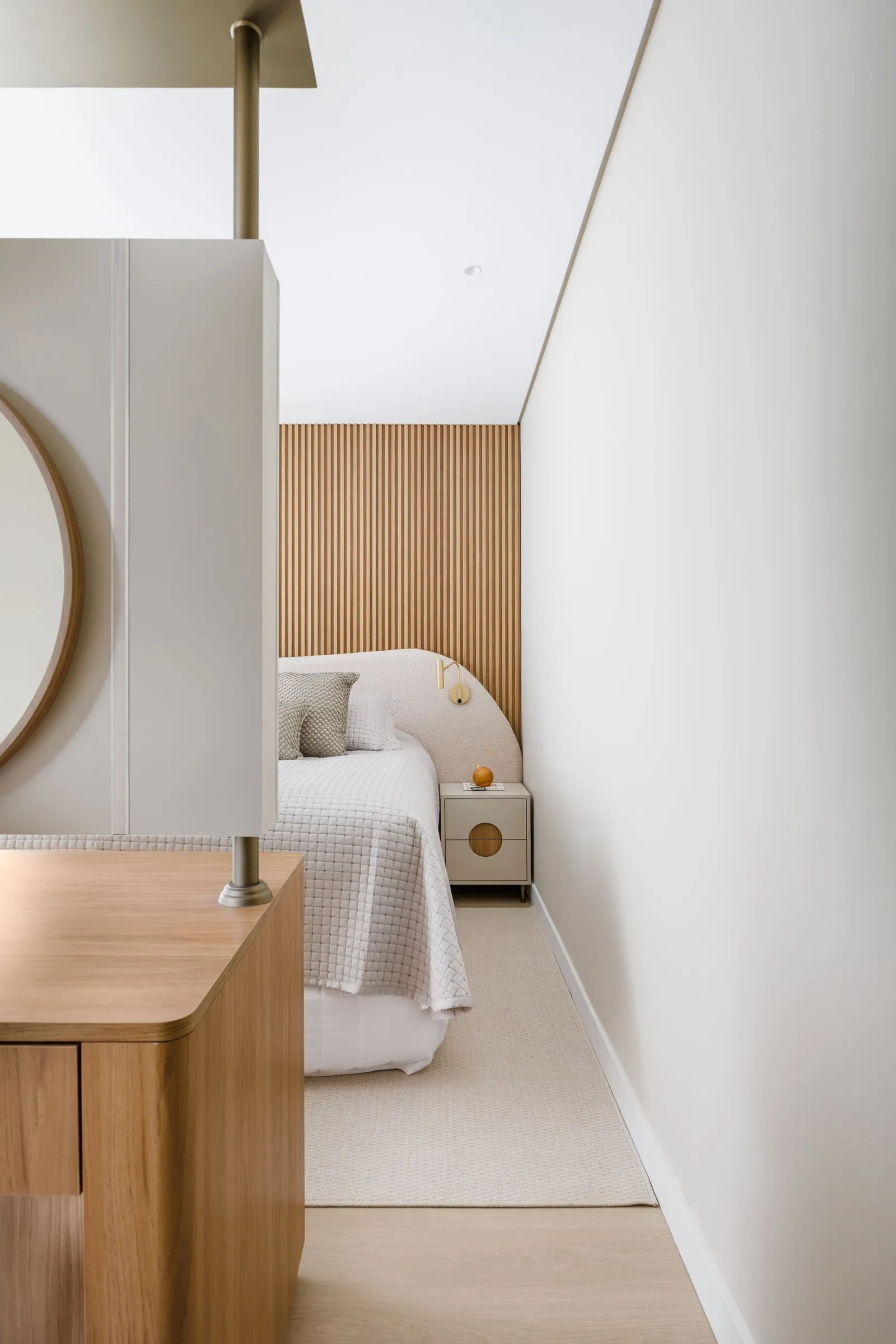 Quarto com cabeceira curva, painel ripado e penteadeira em primeiro plano