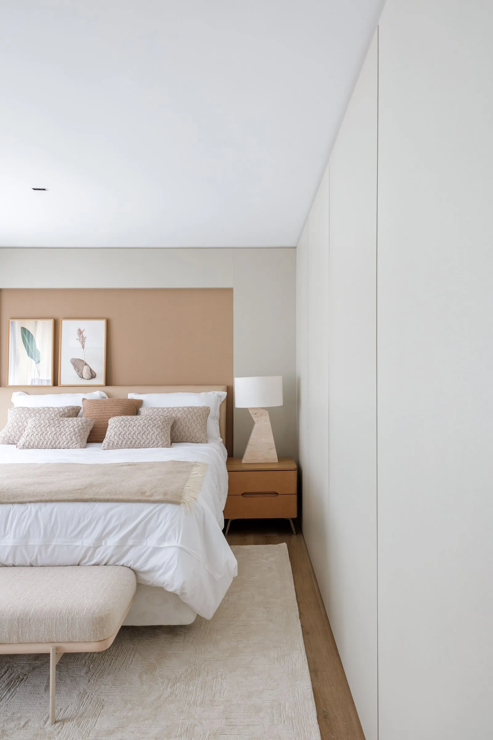 Quarto com cabeceira em painel bege, banco estofado e armário branco