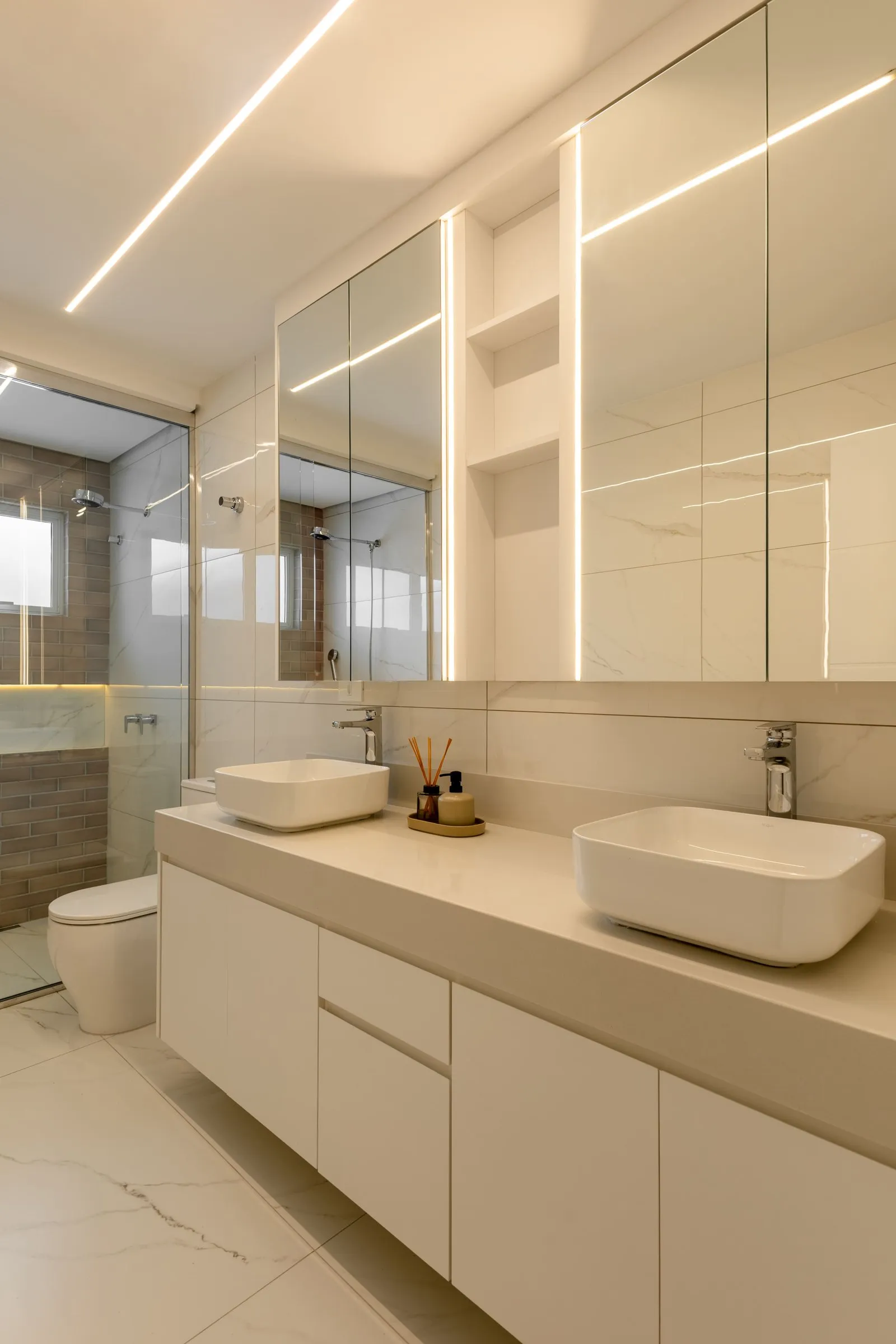 Banheiro com duas cubas de apoio, espelheira com luz e piso de mármore