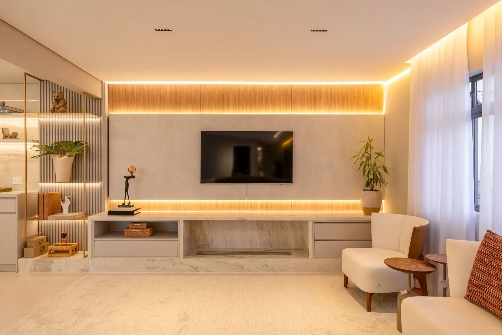 Sala de TV com painel iluminado, rack de mármore e poltronas claras
