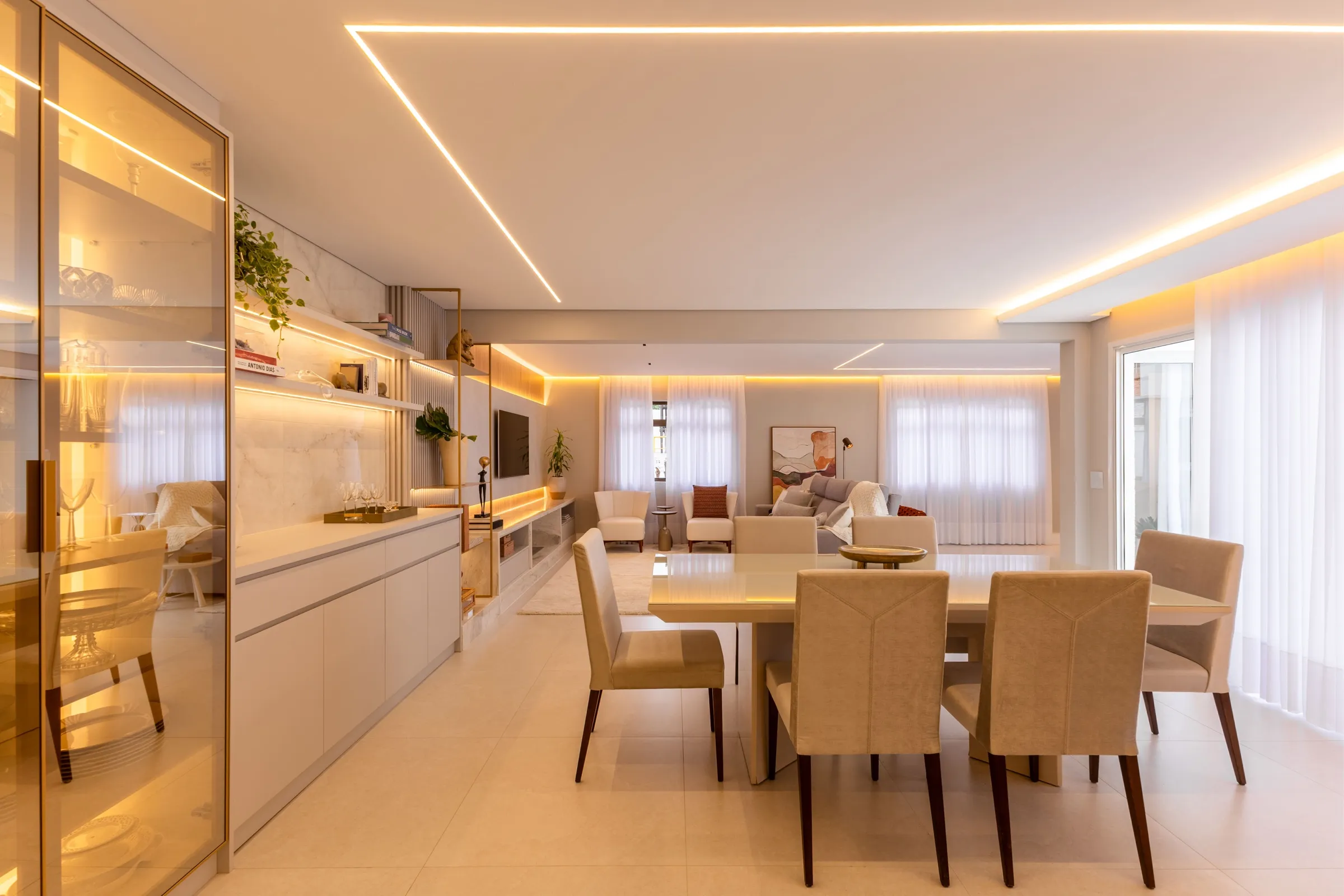 Sala de jantar e estar integradas com cristaleira dourada e fita de luz no teto